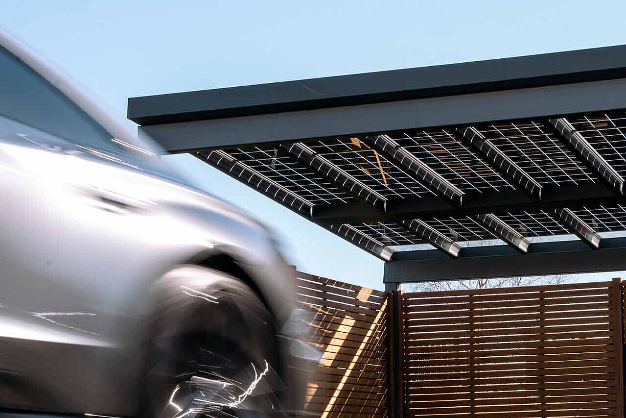Ein Auto fährt gerade in ein umzäuntes Solar Carport 